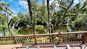 A wooden deck with two blue chairs and a railing overlooking a pond surrounded by trees.