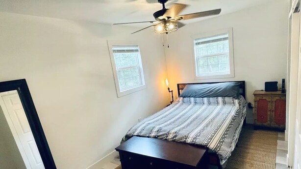 A bedroom with a bed, a ceiling fan, two windows, a nightstand, and a dresser.