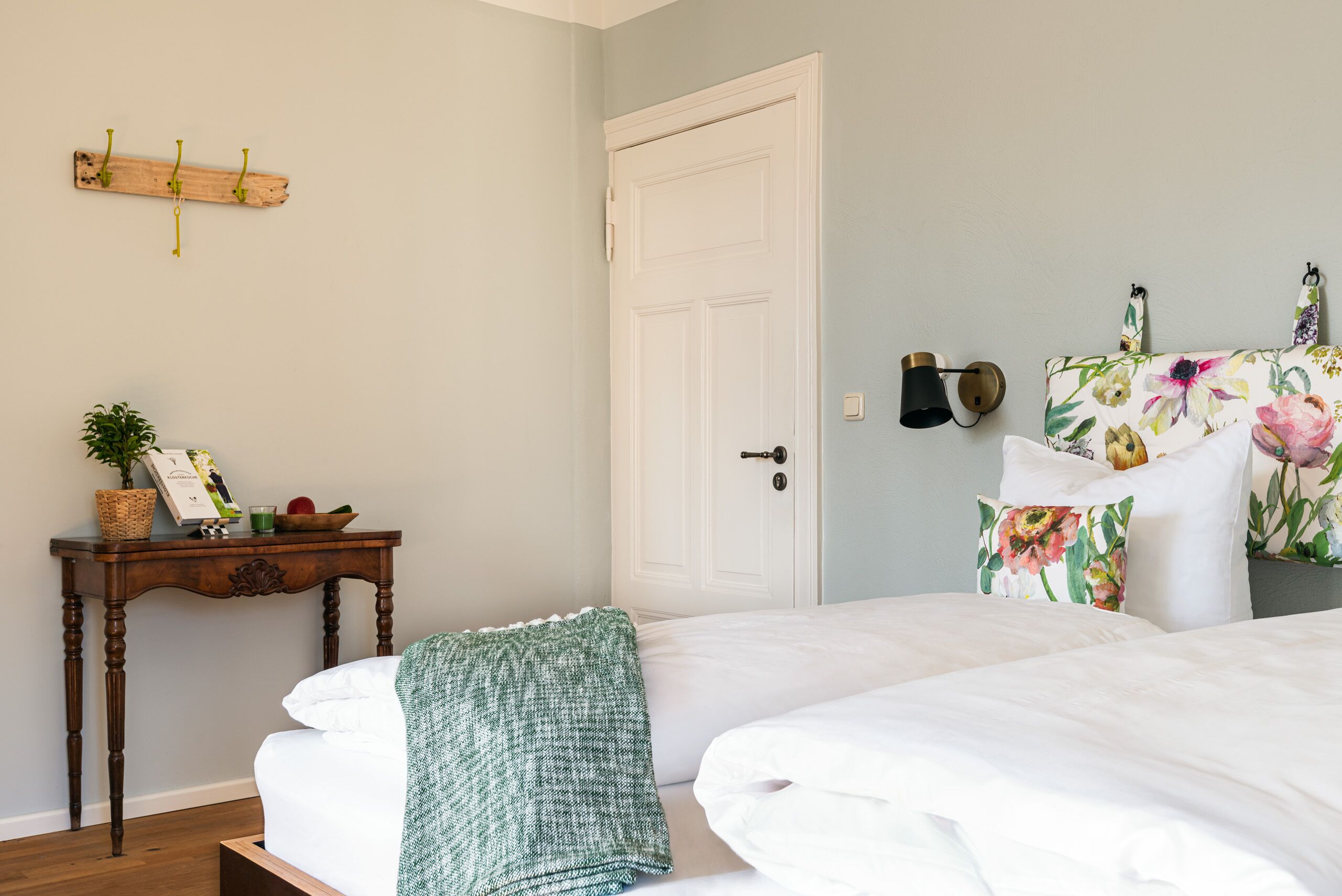 Un dormitorio con cama, una mesita de noche con cesta, una lámpara de pared y una puerta.