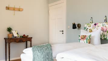 Une chambre à coucher comprenant un lit, une table de chevet avec un panier, un luminaire fixé au mur et une porte.