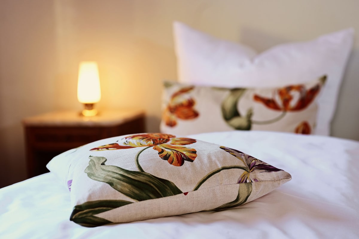 A bed with a floral pillow and a bedside table with a lamp.