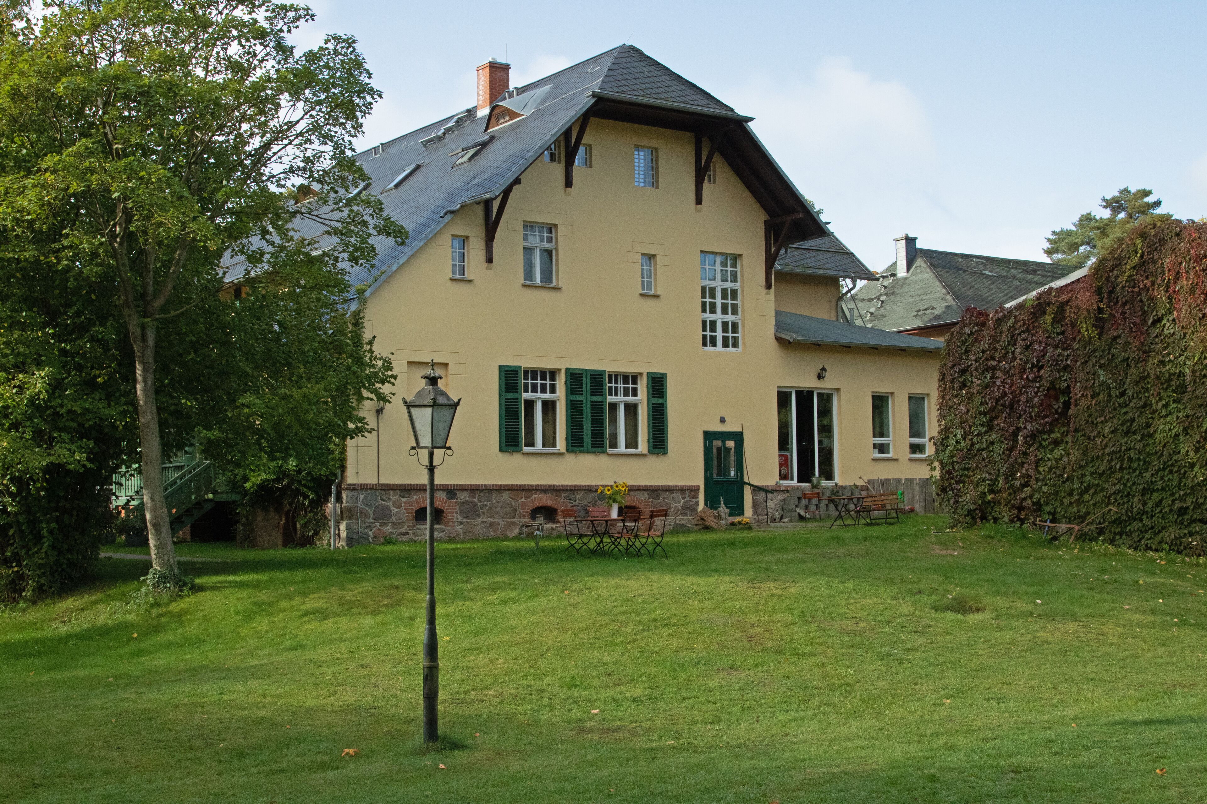 A two-story house with a sloped roof, green shutters, and a stone foundation.