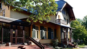 A two-story building with a balcony, a staircase leading to the entrance, and a large tree in front. - Klostergartenhotel Marienfliess (Marienfließ)