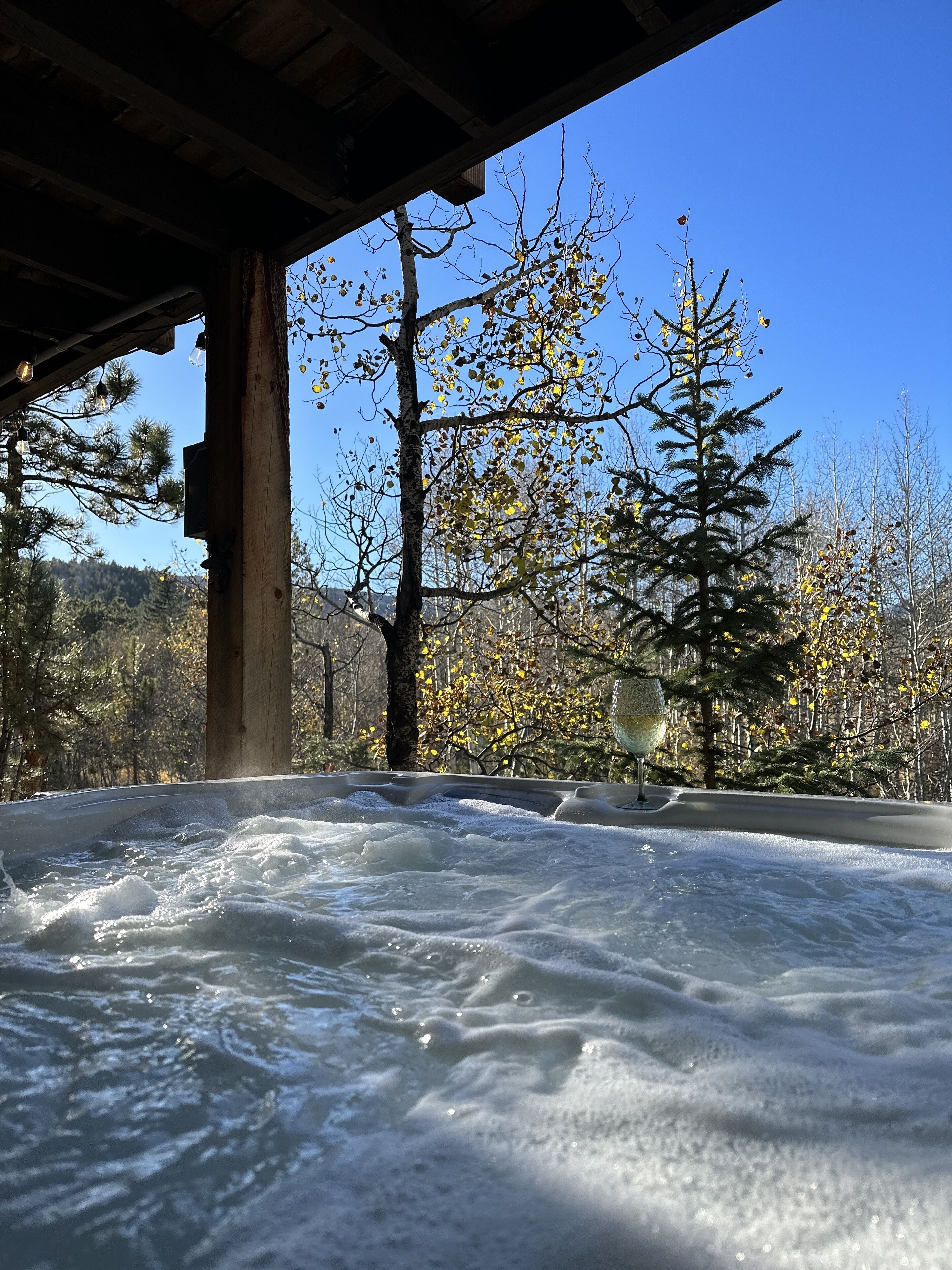 A hot tub under a wooden structure with a clear view of trees and a distant mountain.