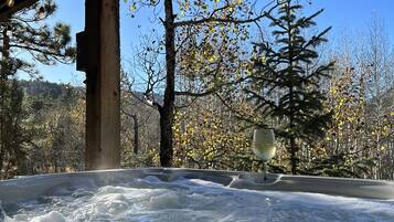 A hot tub under a wooden structure with a clear view of trees and a distant mountain.