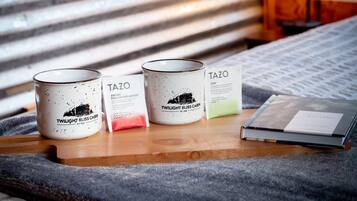 Three TAZO coffee cans on a wooden tray, a book, and a candle on a bed with a striped headboard.