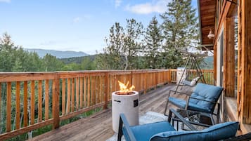 Une terrasse en bois avec un foyer, du mobilier d’extérieur et une vue sur les montagnes.