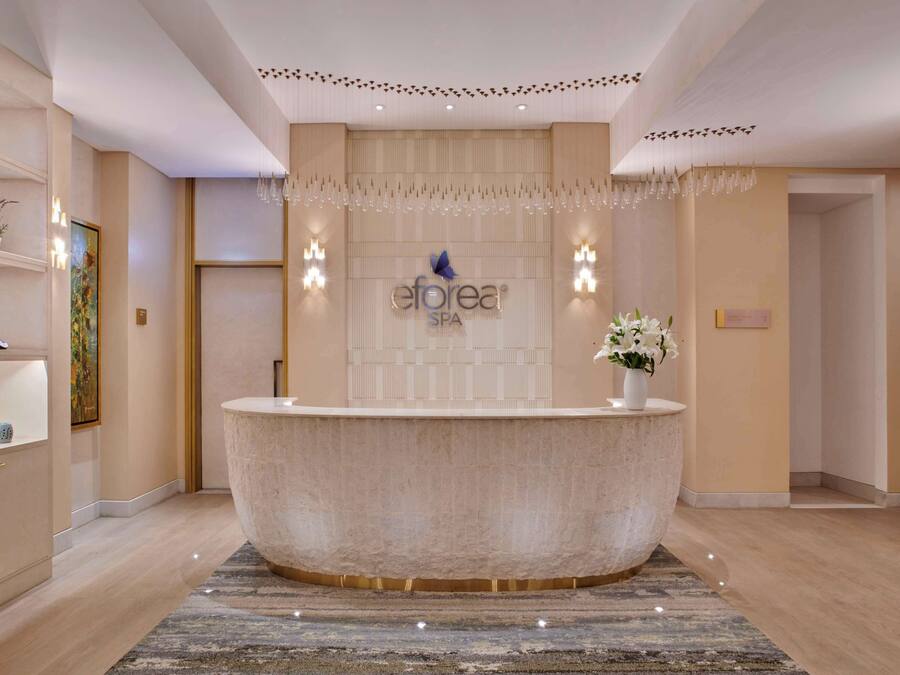Zona de recepción de spa, con un mostrador central, un letrero en la pared y un candelabro decorativo.