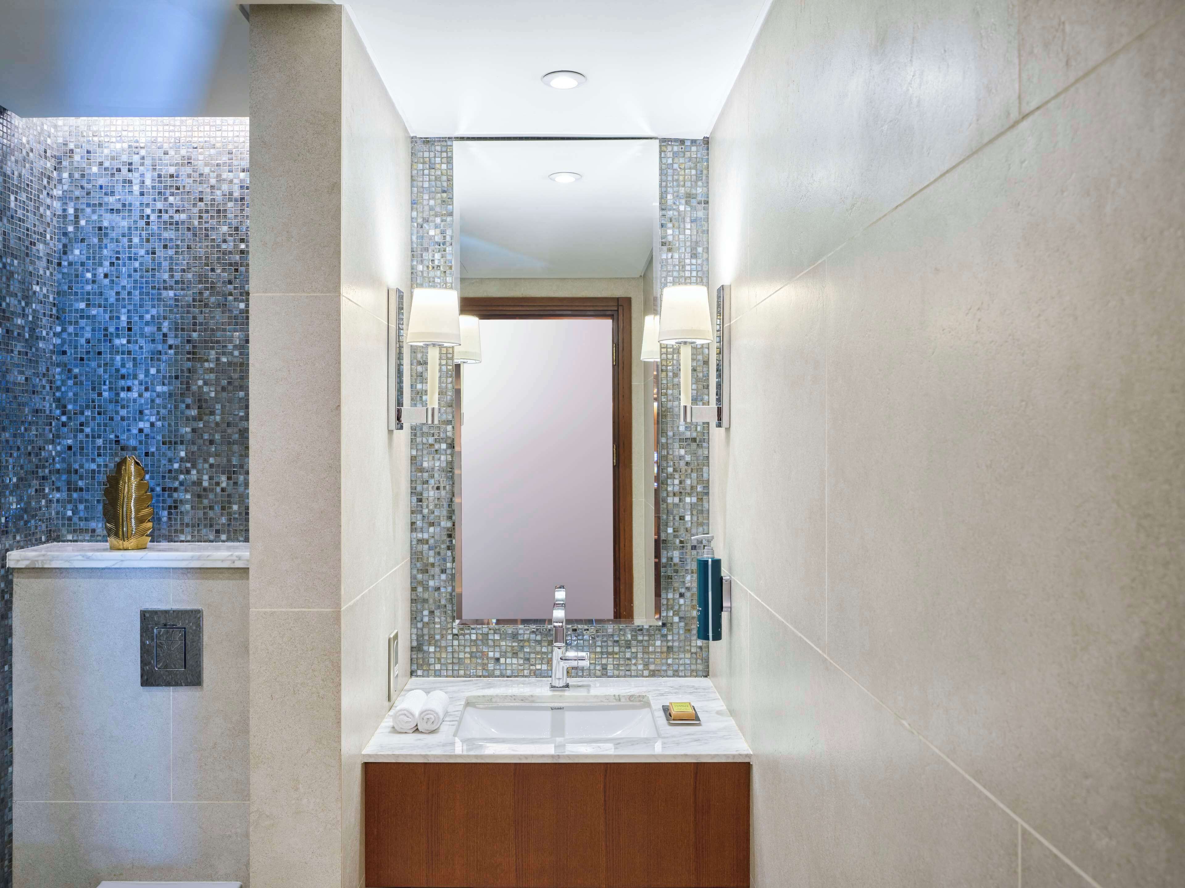 Un baño moderno con un espejo grande, un lavamanos de mármol y una pared de mosaicos.