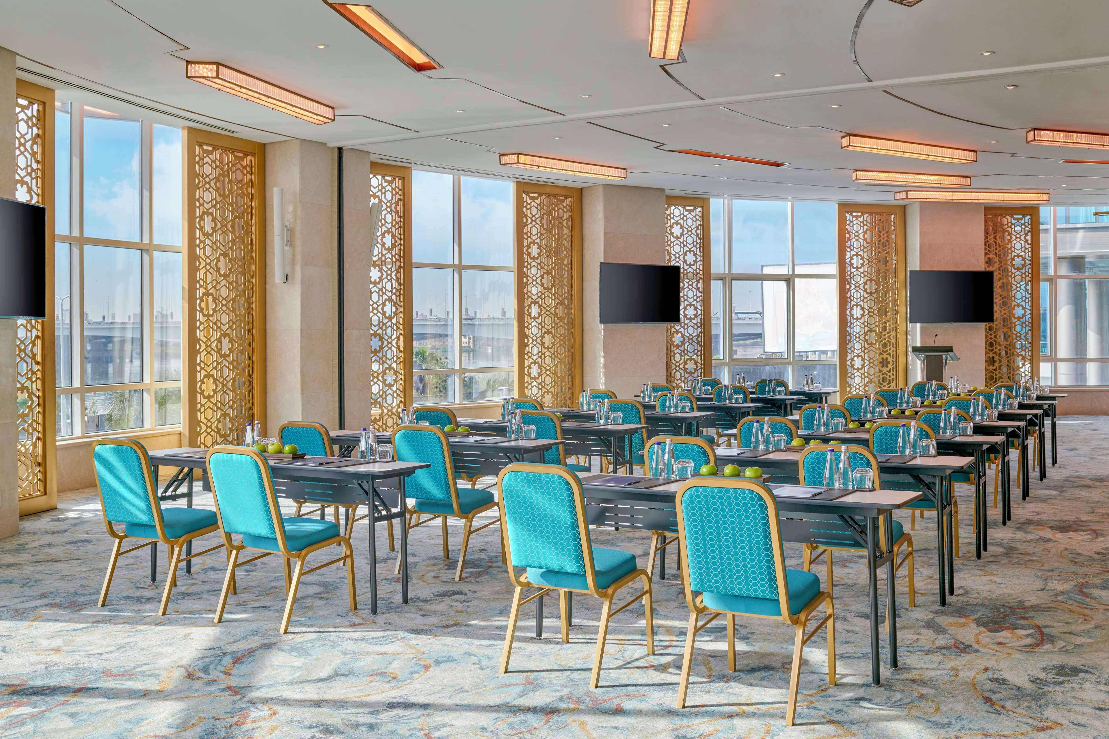 A spacious conference room with rows of tables and chairs, large windows, and modern lighting fixtures.