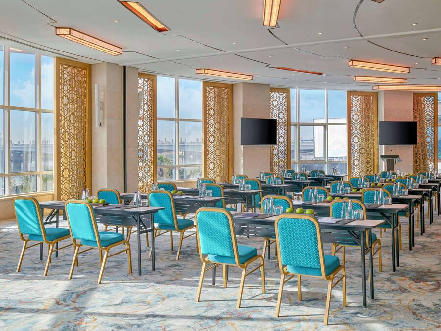A spacious conference room with rows of tables and chairs, large windows, and modern lighting fixtures.