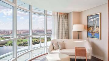 Habitación de hotel moderna con un amplio ventanal que ofrece vistas a la ciudad, un sofá cómodo, una pequeña mesita de madera y un cuadro en la pared.