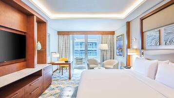 Ein Hotelzimmer mit einem großen Bett, einem Fernseher, einem Schreibtisch mit Stuhl und Blick ins Freie.