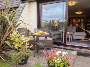 A patio with wicker furniture, a glass door leading to an interior living area, and potted plants. - Pavey Ark (Ambleside)