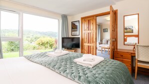 Quarto de hotel com cama grande, televisão, escrivaninha com espelho e vista para o exterior.