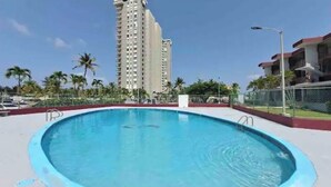 A swimming pool surrounded by a fence, with tall buildings in the background. - Brand New Modern Studio with Pool (Luquillo)