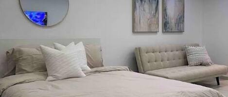 Une chambre à coucher moderne avec un grand lit, un miroir rond et deux œuvres d’art accrochées au mur.