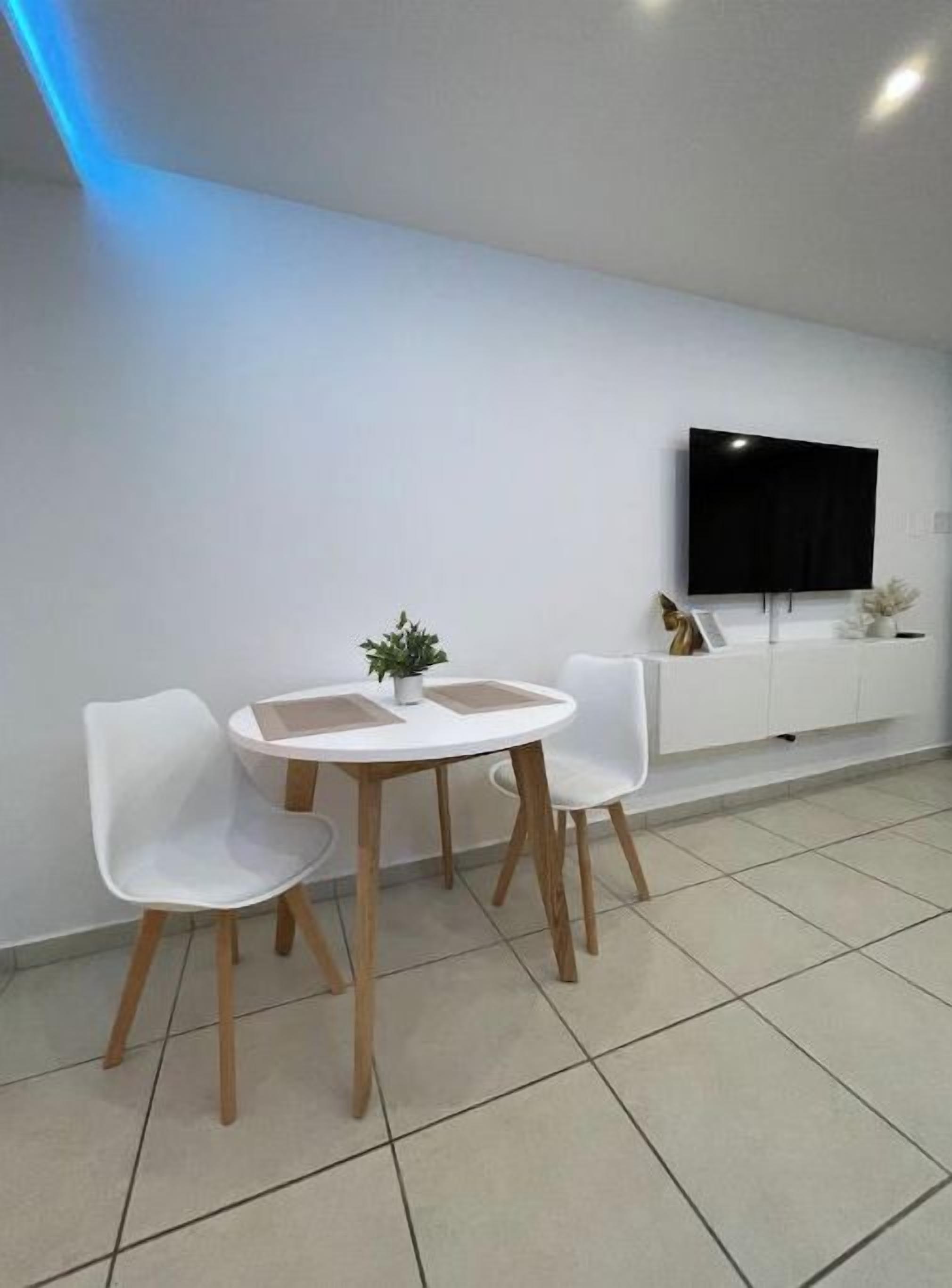 A modern, minimalist room with a white wall, a flat-screen TV mounted above a white console, and a small table with two white chairs.