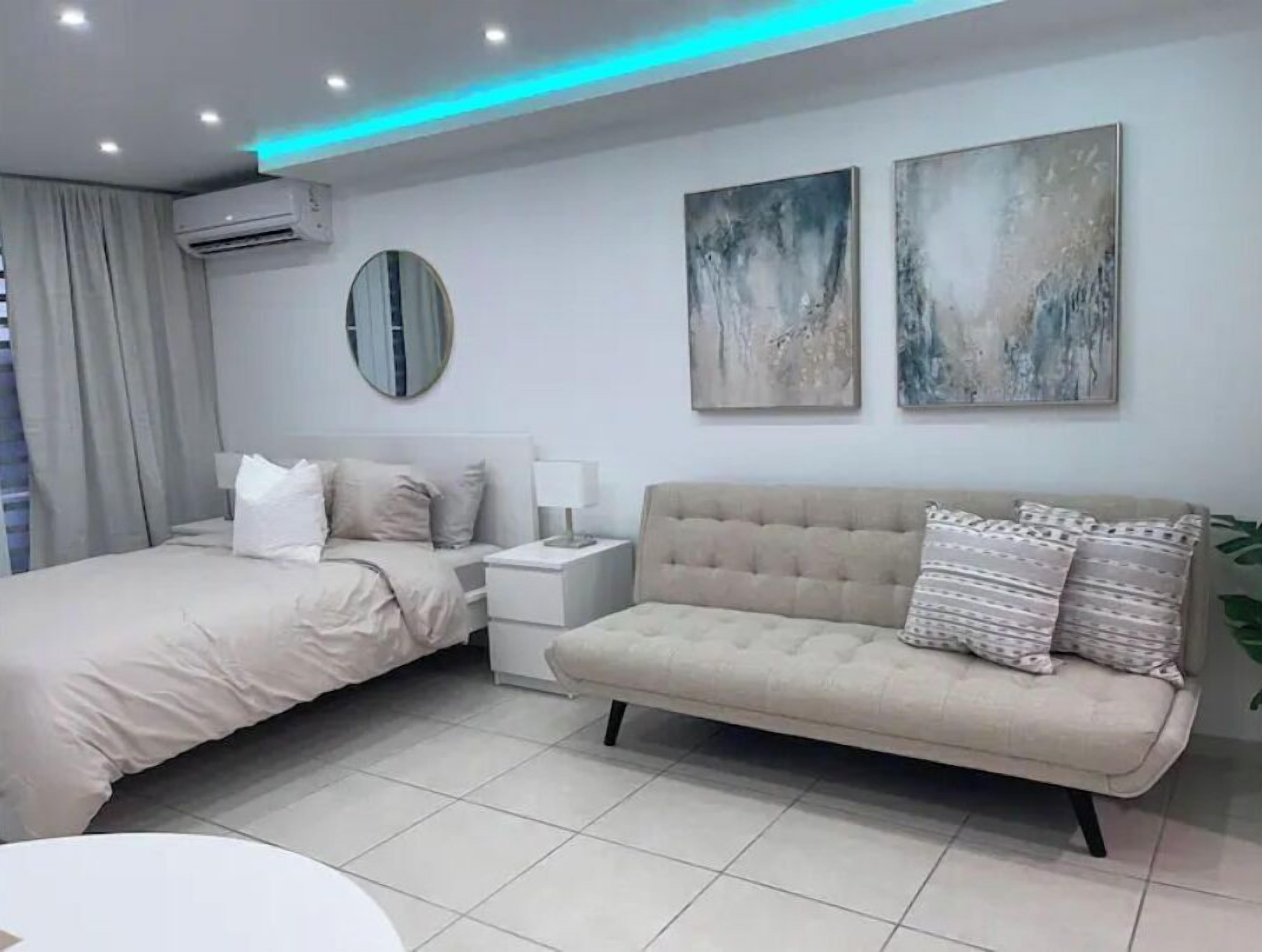 Une chambre moderne comprenant un lit, un canapé, une table de chevet, un climatiseur et deux tableaux abstraits accrochés au mur.
