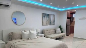 A modern bedroom with a large bed, bedside tables, a round mirror, and abstract wall art. - Brand New Modern Studio with Pool (Luquillo)