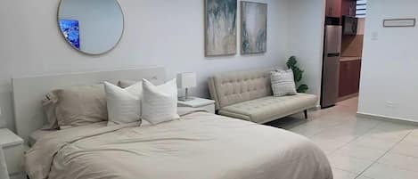 A modern bedroom with a large bed, bedside tables, a round mirror, and abstract wall art.