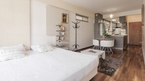 A modern bedroom with a large bed, bedside tables, a desk, and a kitchenette. - Departamento moderno (Buenos Aires)