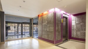 A modern elevator area with a glass door, a purple wall, and a tiled floor. - Departamento moderno (Buenos Aires)