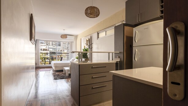 A modern kitchen with a built-in refrigerator, a dining area with a white table and chairs, and a view of a balcony with outdoor furniture. - Departamento moderno (Buenos Aires)