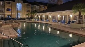 Zona de piscina con sillones de descanso y un edificio con amplias ventanas y balcones.