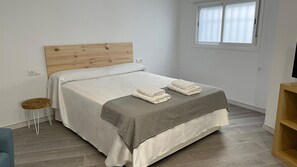 Ein ordentlich bezogenes Bett mit einem hölzernen Kopfteil, einer grauen Decke und zwei gefalteten Handtüchern.
