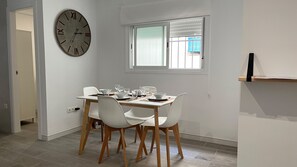 Ein Essbereich mit einem Tisch für vier Personen, einer Wanduhr und einem Fenster mit Jalousien.