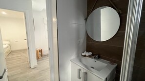 Ein modernes Badezimmer mit rundem Spiegel, weißem Waschbecken und Holzboden.