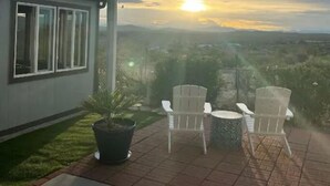 A patio with two white chairs and a table, overlooking a cityscape during sunset. - Elephant Lake Summerset Oasis New (Elephant Butte)