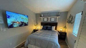 A bedroom with a large bed, a mounted TV, a nightstand with a lamp, and a decorative shelf above the bed. - Elephant Lake Summerset Oasis New (Elephant Butte)