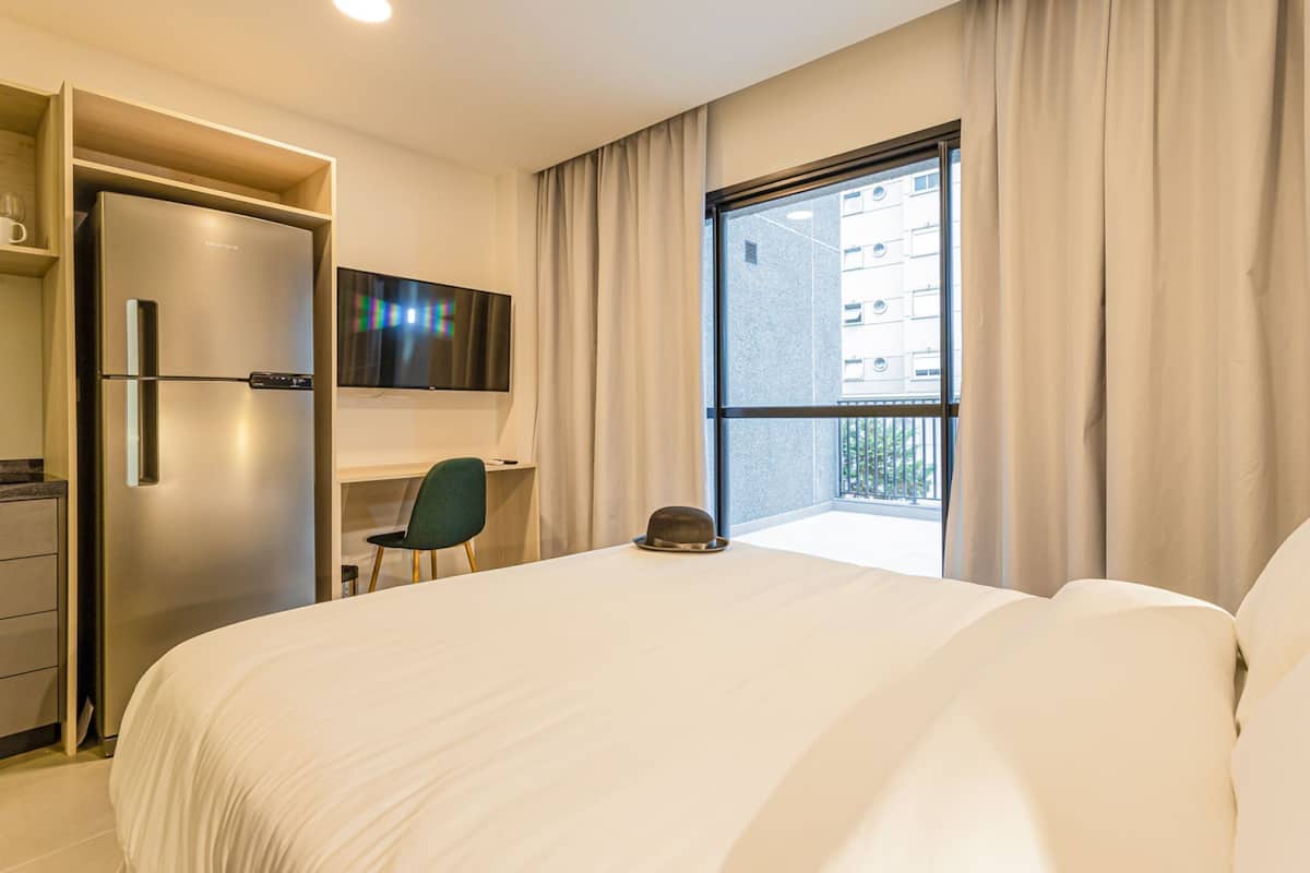 Une chambre d’hôtel avec un lit, un bureau, une télévision, une fenêtre avec des rideaux et une porte.