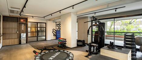 A modern gym with various exercise equipment, a wooden bench, and a large window offering a view of greenery.