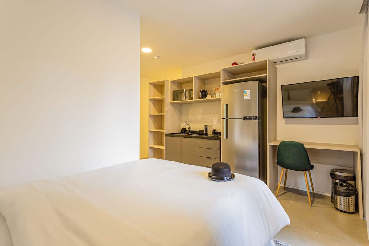 Une chambre d’hôtel comprenant un lit, un bureau avec une chaise, une kitchenette et un téléviseur.