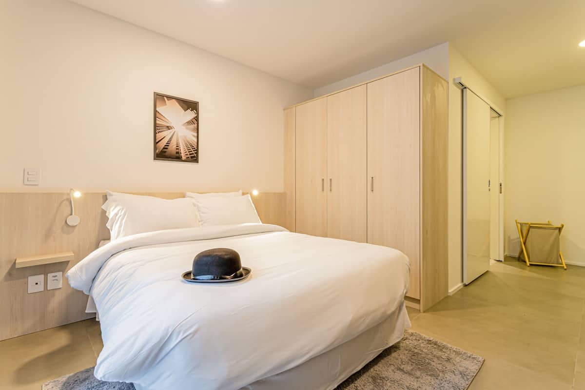 Une chambre moderne avec un grand lit, une armoire et une petite table sur laquelle est posé un chapeau.