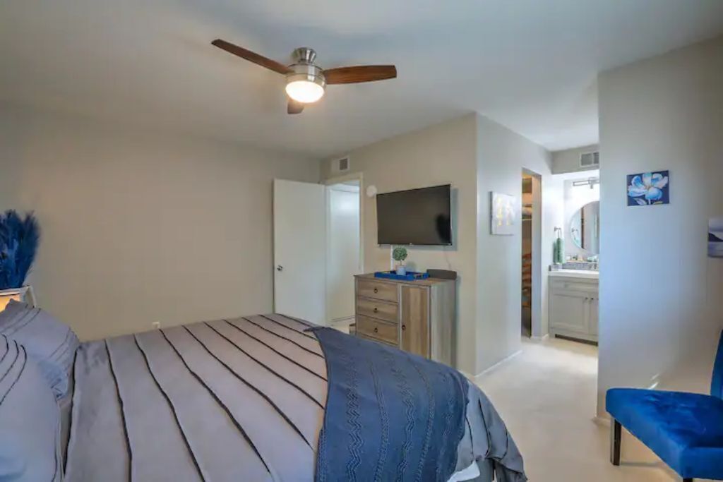 Un dormitorio con una cama, ventilador de techo, cómoda, televisor y una silla.