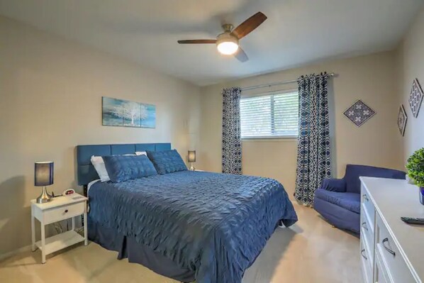 A bedroom with a bed, a nightstand, a ceiling fan, a window with patterned curtains, and a blue sofa.