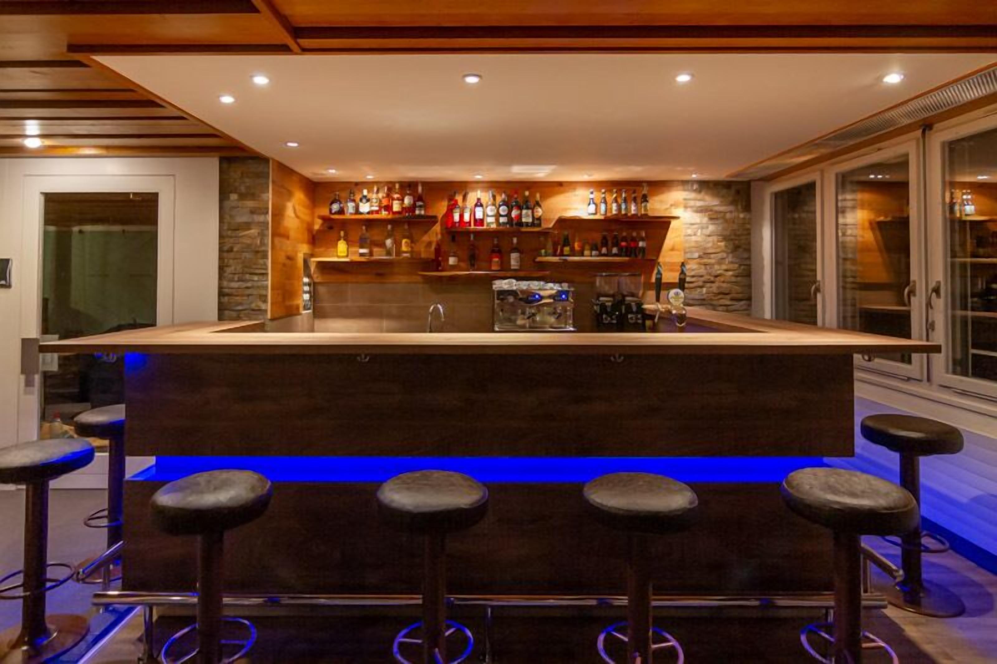 Eine Bar mit einer zentralen Theke, Hockern und Regalen voller Flaschen.