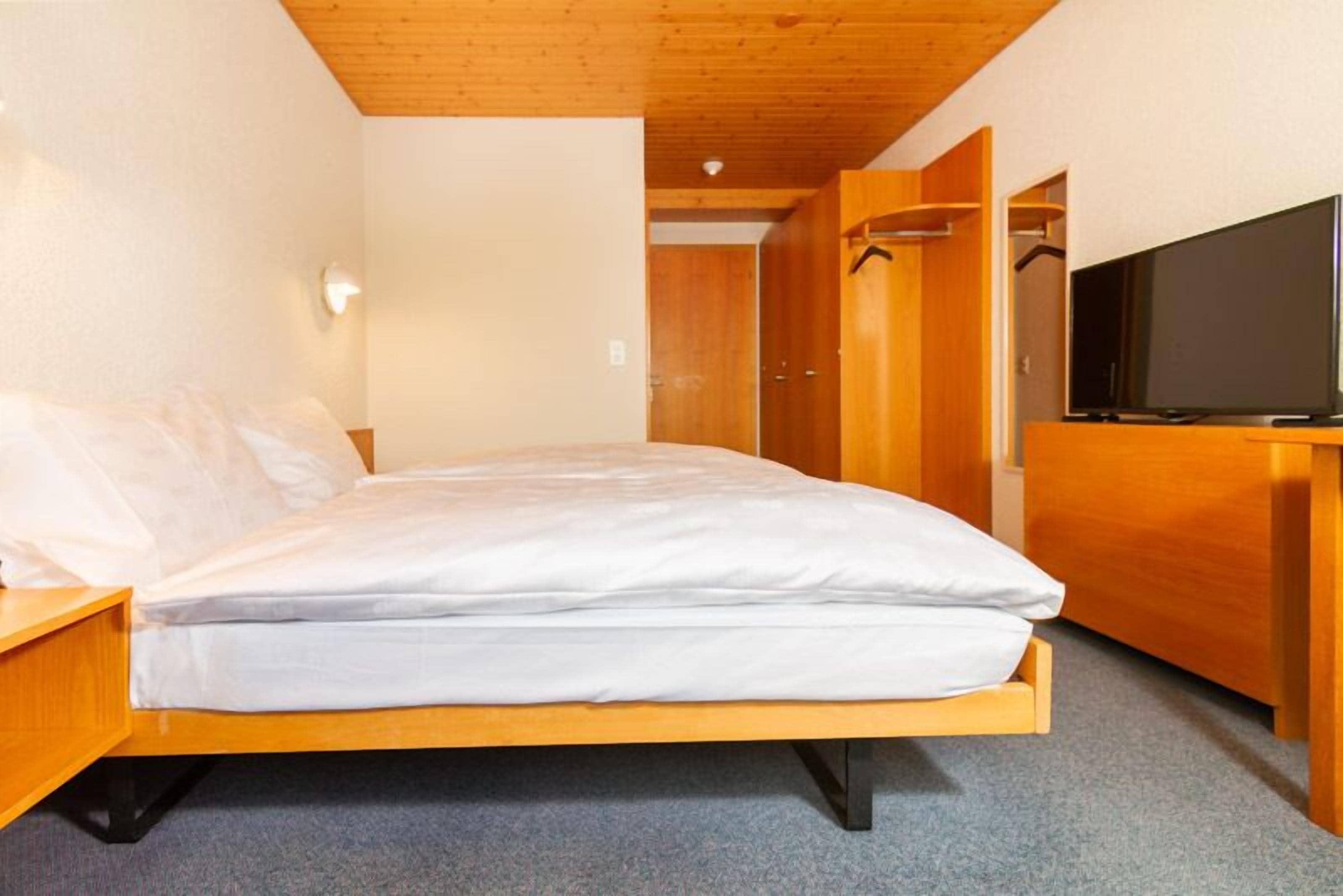 Un lit simple avec un cadre en bois et une literie blanche, dans une pièce dont le plafond et les murs sont en bois.