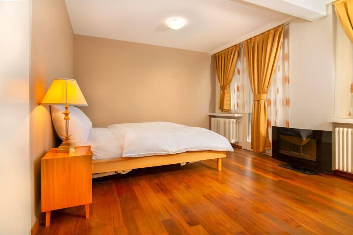 Ein Schlafzimmer mit Bett, Nachttisch, Lampe, Kamin und Vorhängen.