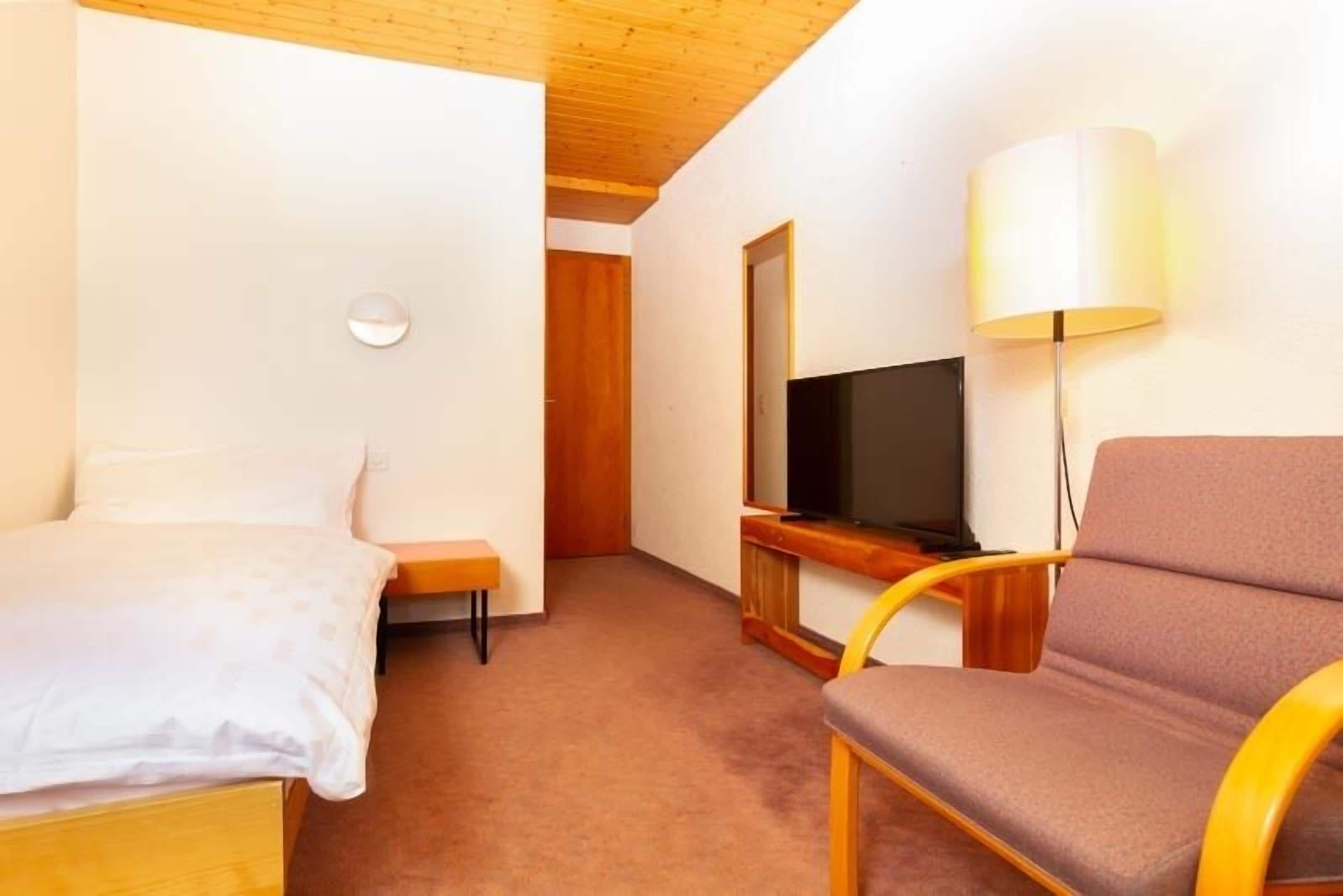Una habitación de hotel con cama, silla, televisión y lámpara.