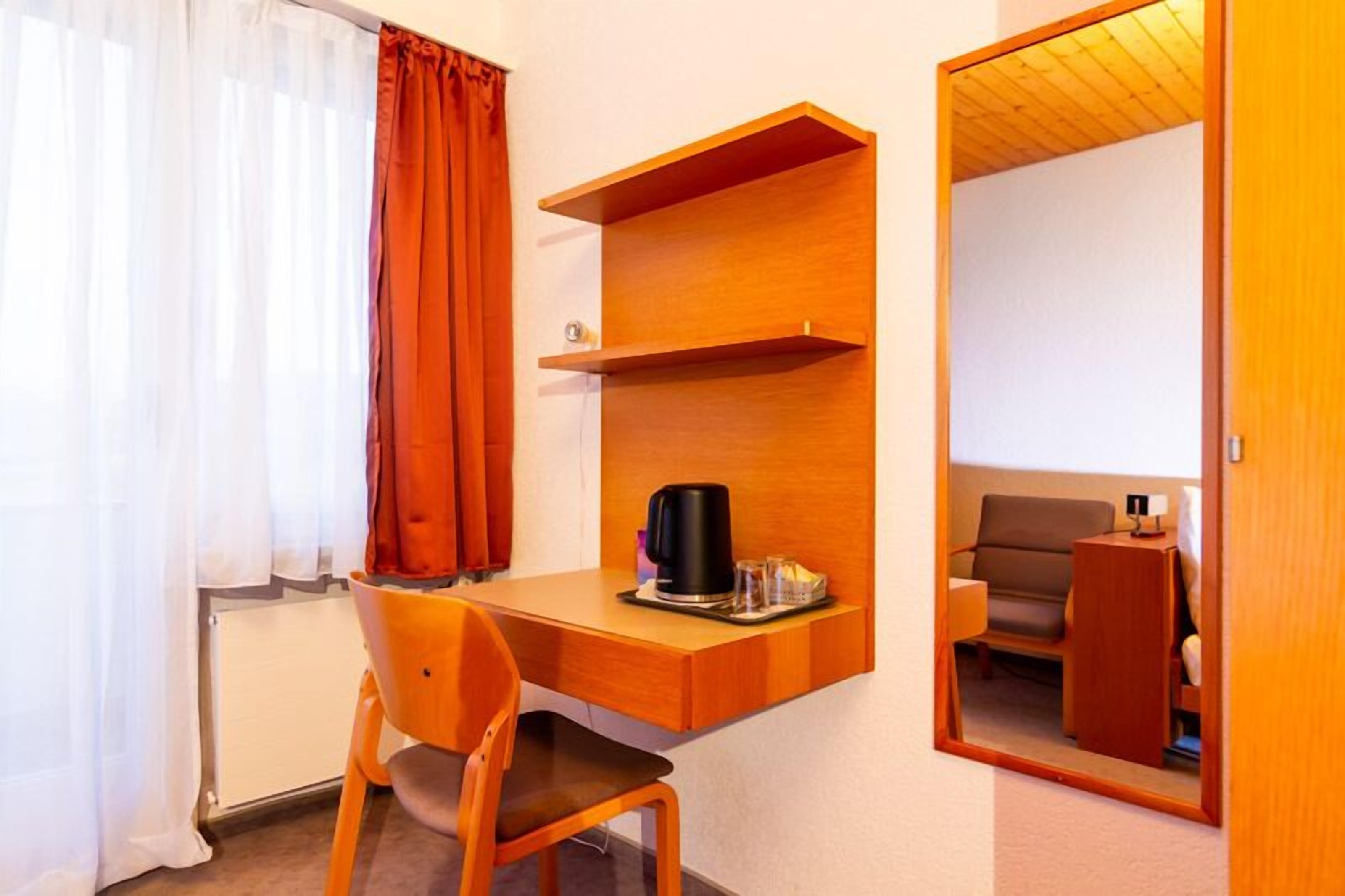A compact room with a wooden desk, a chair, a coffee maker, and a sofa.