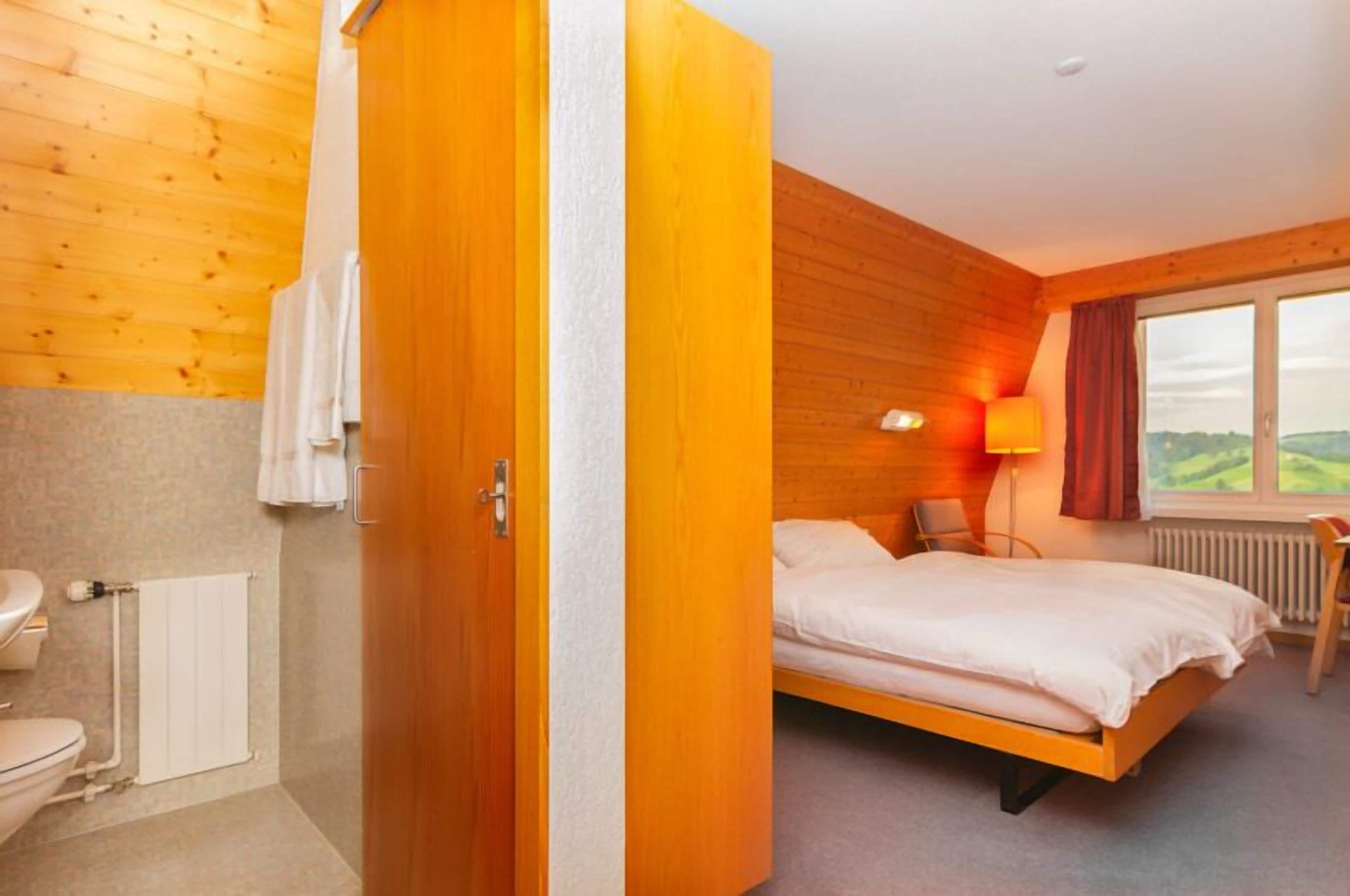 A bedroom with a wooden bed, a nightstand, a lamp, and a window with a view.