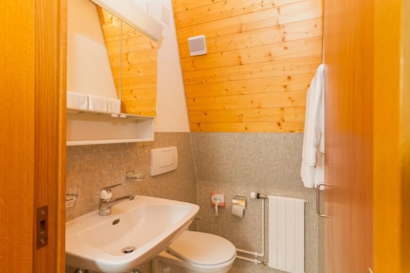 Un baño pequeño con pared de madera, lavamanos blanco y un inodoro.