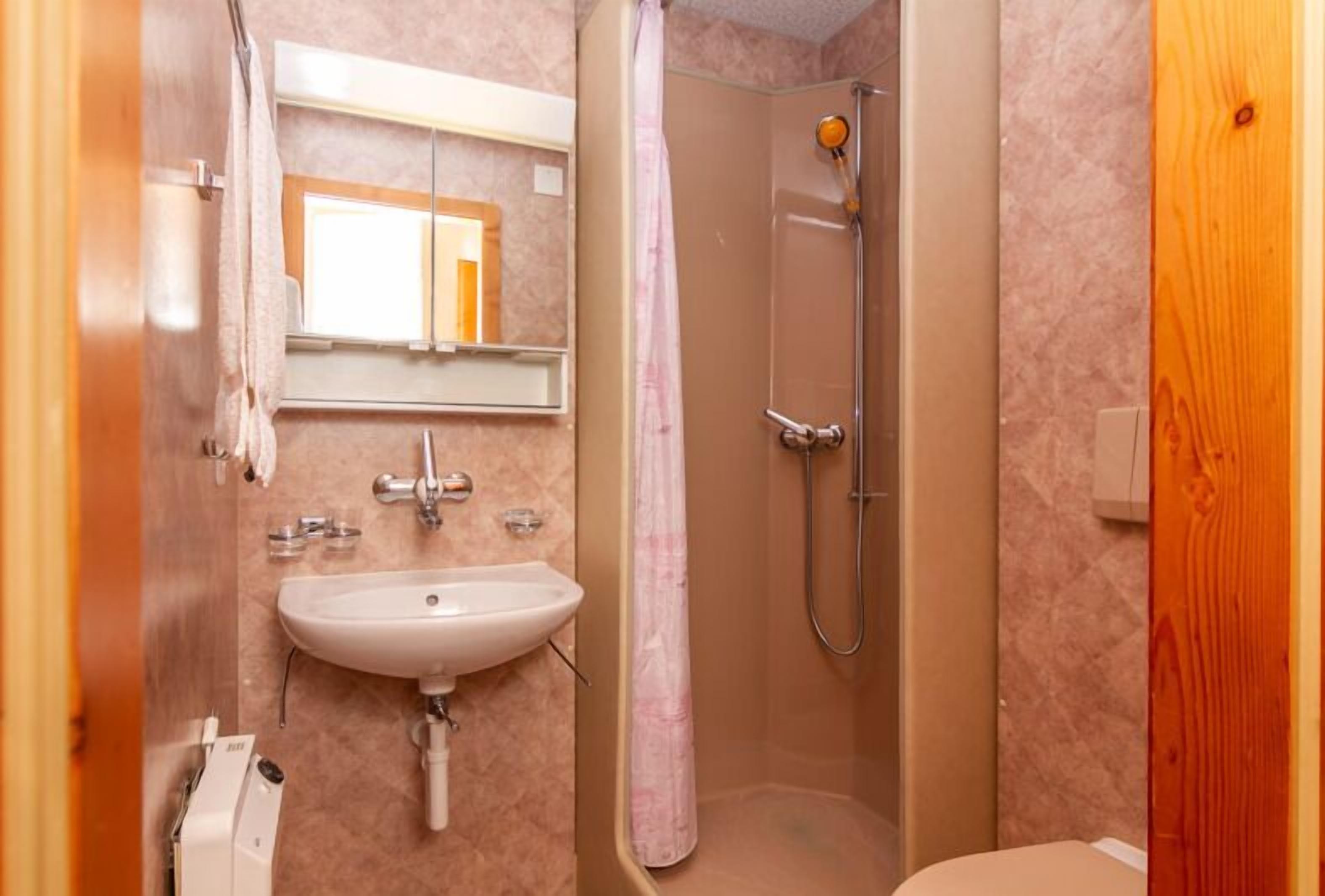Un baño con lavabo, espejo, ducha y puerta de madera.