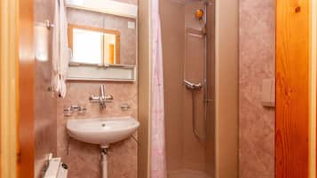 Un baño con lavabo, espejo, ducha y puerta de madera.