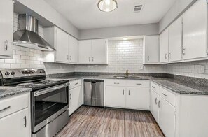 A modern kitchen with white cabinets, a stainless steel range hood, a dishwasher, and a granite countertop.